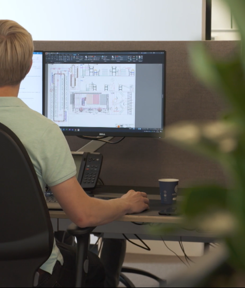 Employee sitting behind 2 monitors with technical drawing of sorter