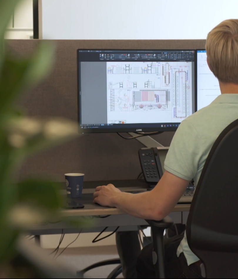 Employee sitting behind two monitors with technical drawing of sorter.