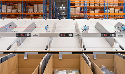 Image of a Push Tray Sorter with sliding chutes that include the Chute Pitch Reducer and cardboard boxes at the end of the chute.